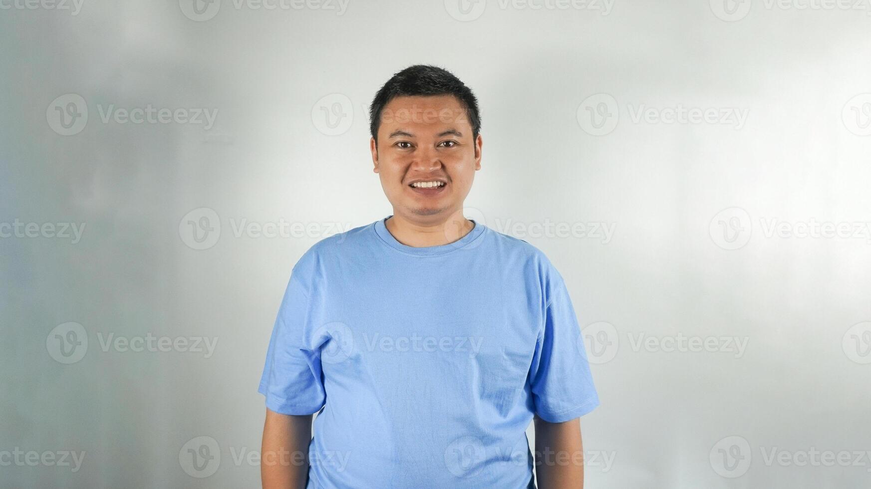 A young Indonesian man wearing a blue t-shirt with a smiling face facing forward photo