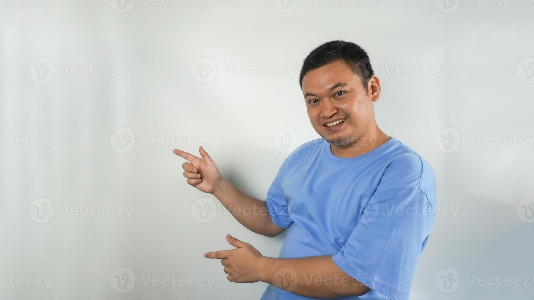 A young Indonesian man wearing a blue t-shirt with a happy face pointing to the right photo