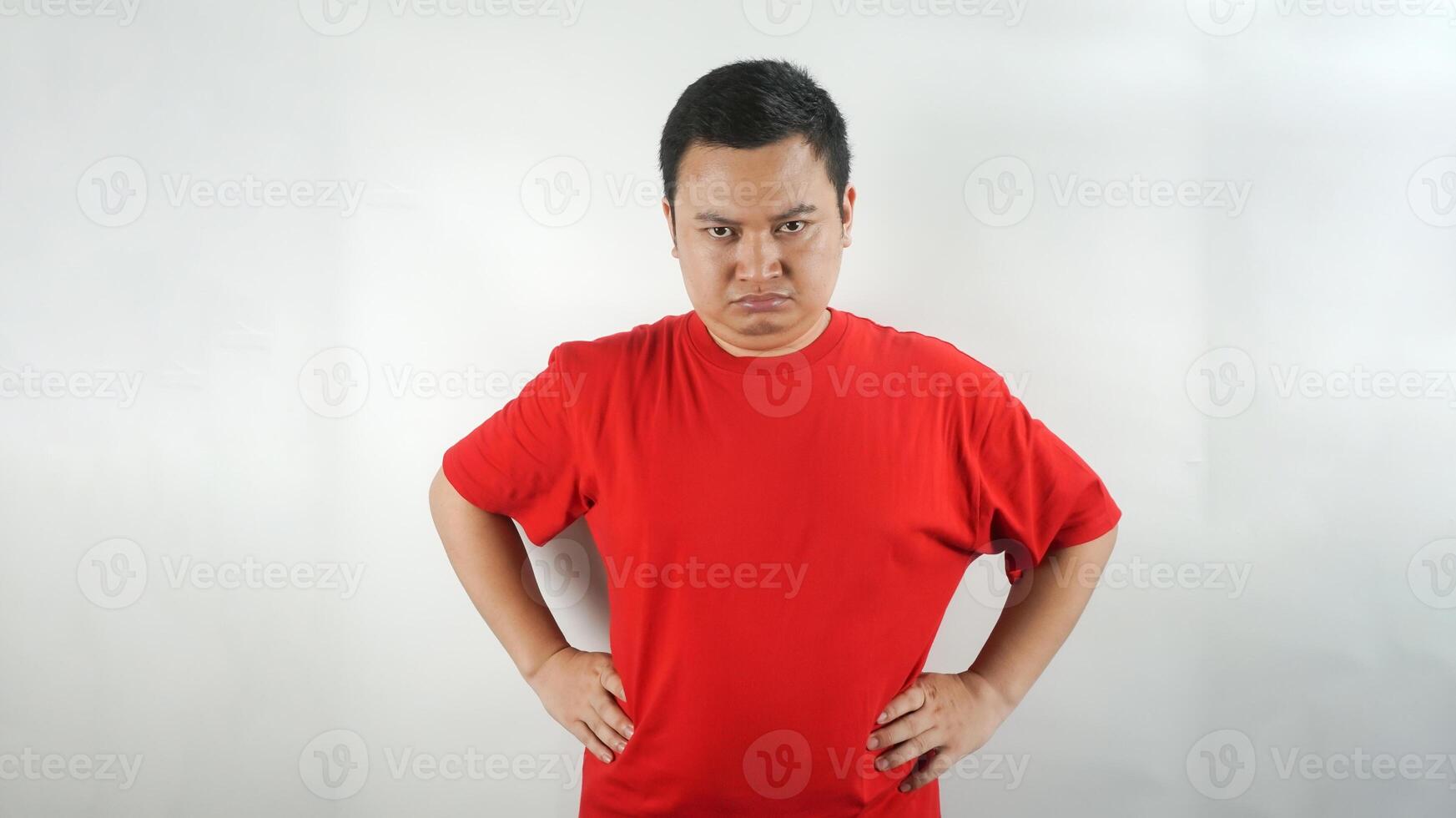 A young Indonesian man wearing a red t-shirt with a frown facing forward photo
