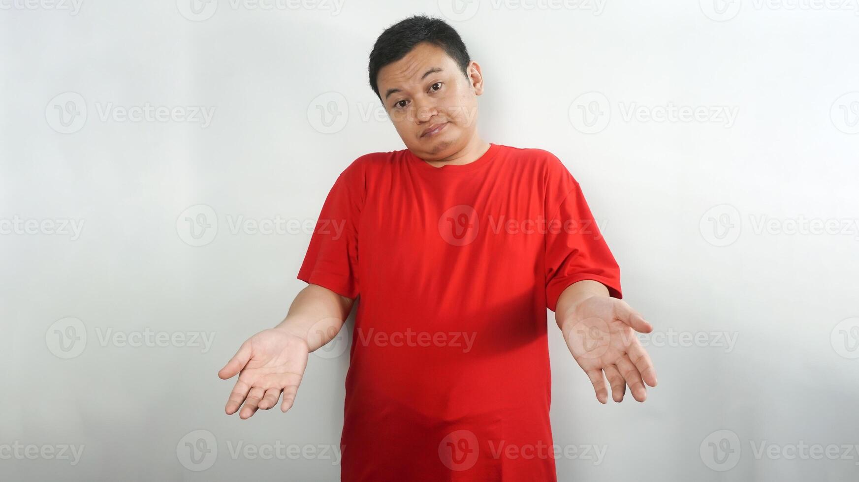 A young Indonesian man wearing a red t-shirt with a confused face facing forward photo