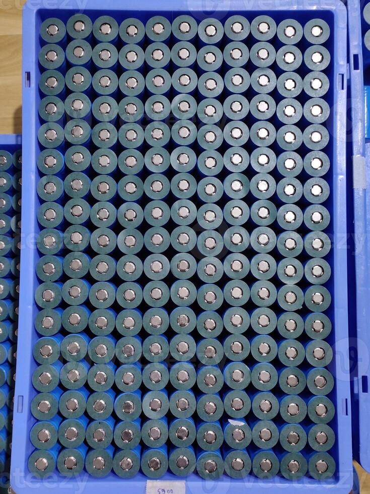 A top-down view of a blue plastic tray filled with cylindrical lithium-ion batteries arranged in a neat grid. Each silver-cased battery shows its black top and blue base, positive terminal up. photo
