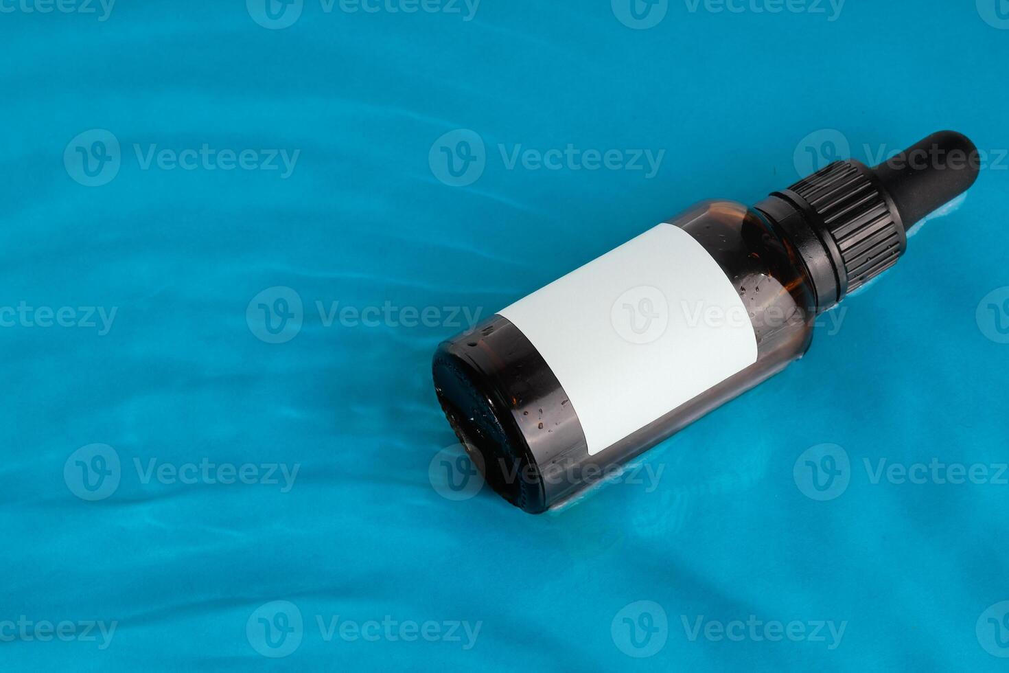 Amber glass dropper bottle with a blank label floating on a blue water surface ideal for branding mockups photo
