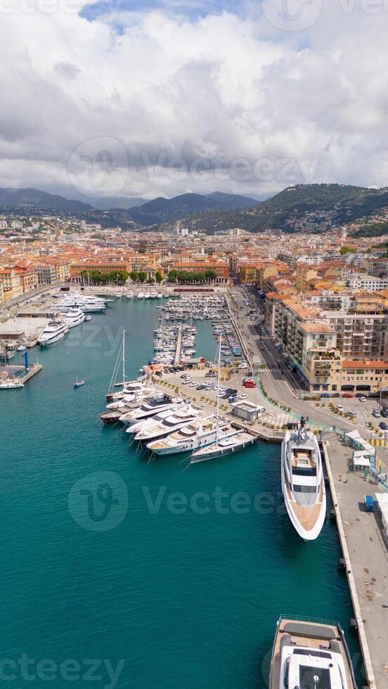 Aerial view of Nice, France, showcasing the vibrant port filled with luxury yachts and turquoise waters, with the city's colorful buildings and surrounding hills in the background photo