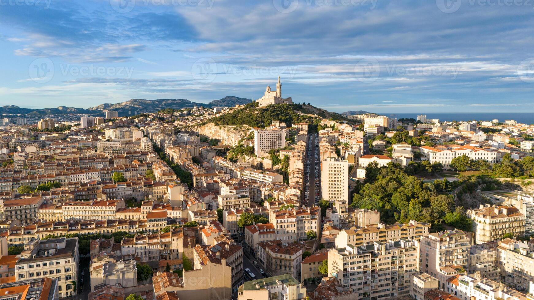 Aerial view of Marseille, France, featuring rooftops, streets, and the Notre-Dame de la Garde basilica, with the Mediterranean Sea in the background. photo
