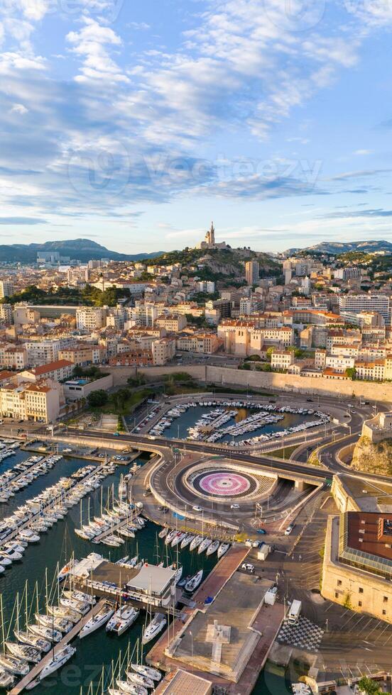 Aerial view of Marseille, France, featuring the vibrant port with yachts, the historic Fort Saint-Nicolas, and the iconic Notre-Dame de la Garde basilica atop the hill. photo
