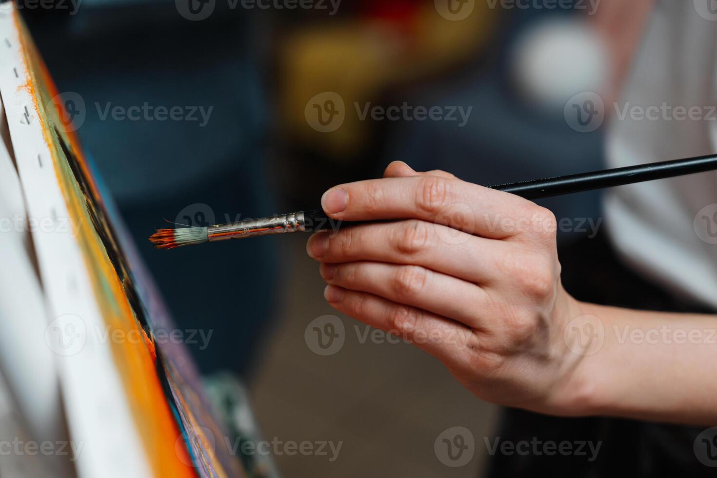 A close-up of an artists hand painting on canvas with a brush in a studio photo