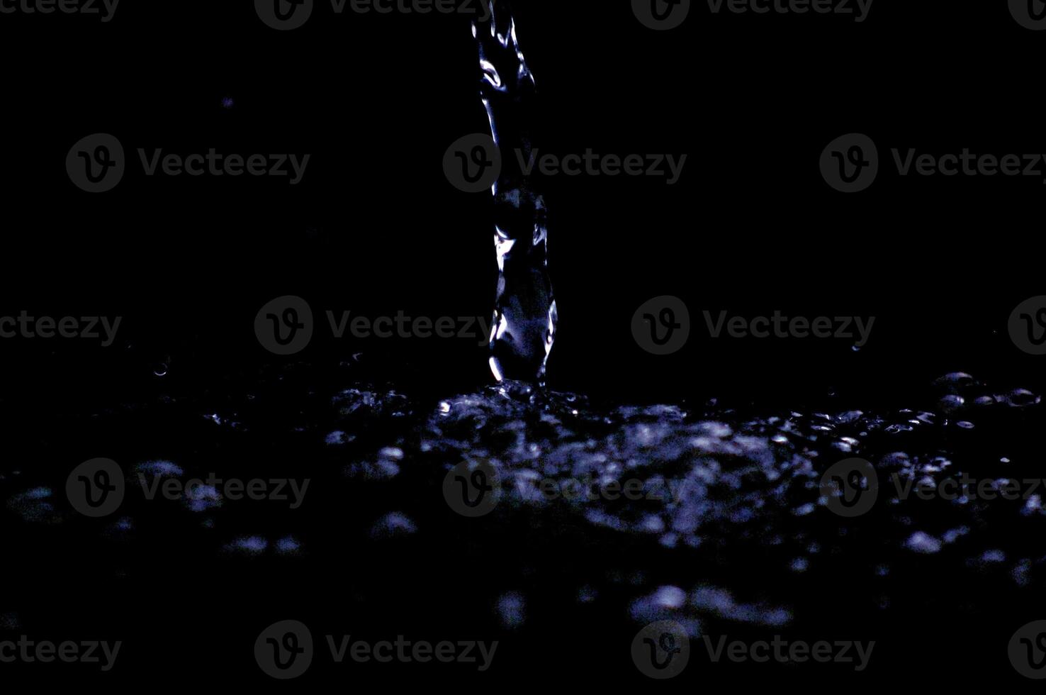 Water stream the air in dark. Splashing water fly in the air. Part of the drops is in focus, part - out of the focus. photo