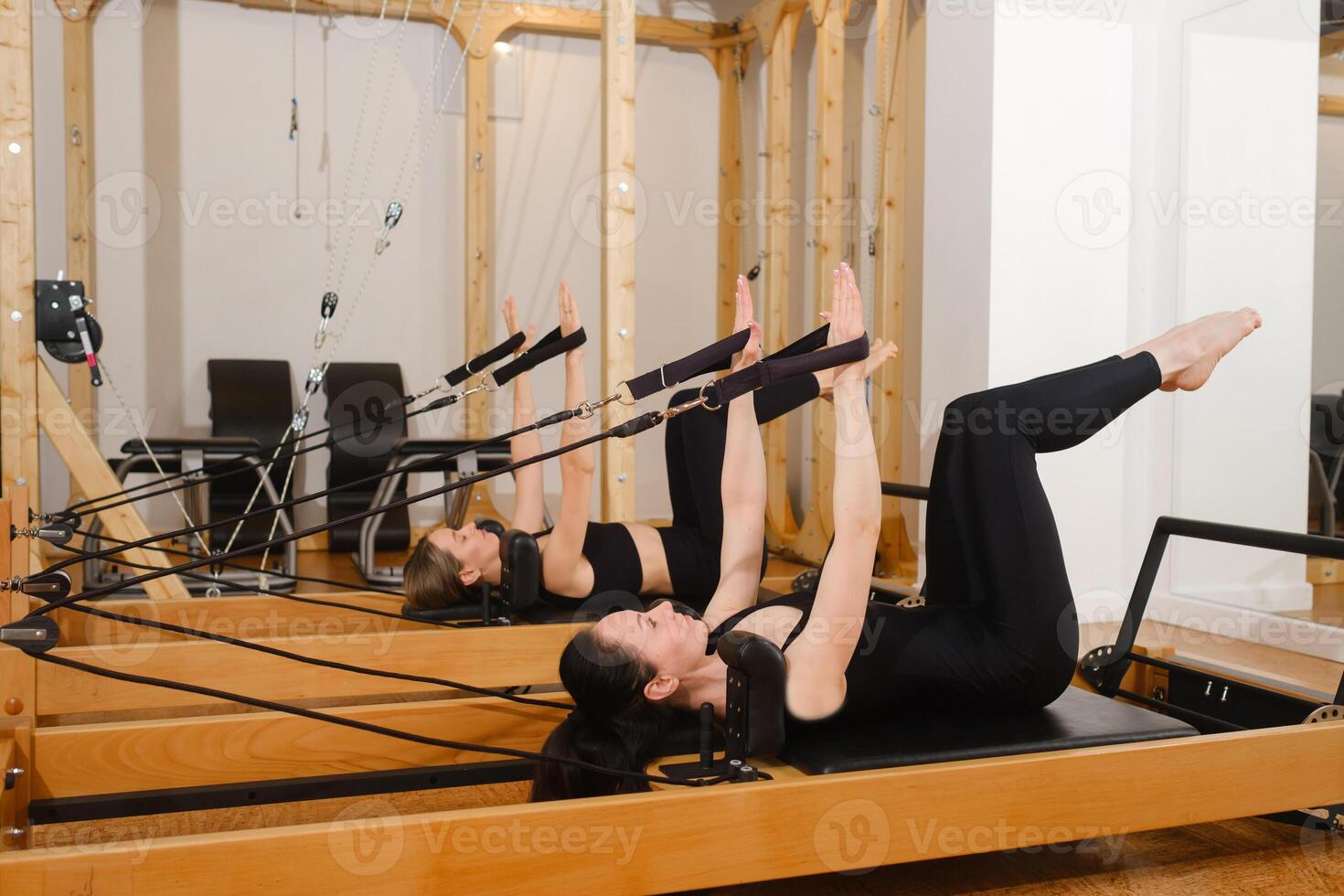 Two women in black sportswear are doing pilates on a reformer machine in the gym photo