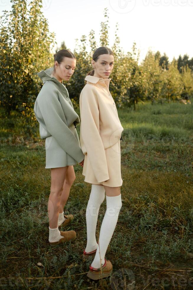 Two models in stylish tracksuits pose in apple orchard at sunset . The model is wearing a light-colored tracksuit and skirt photo