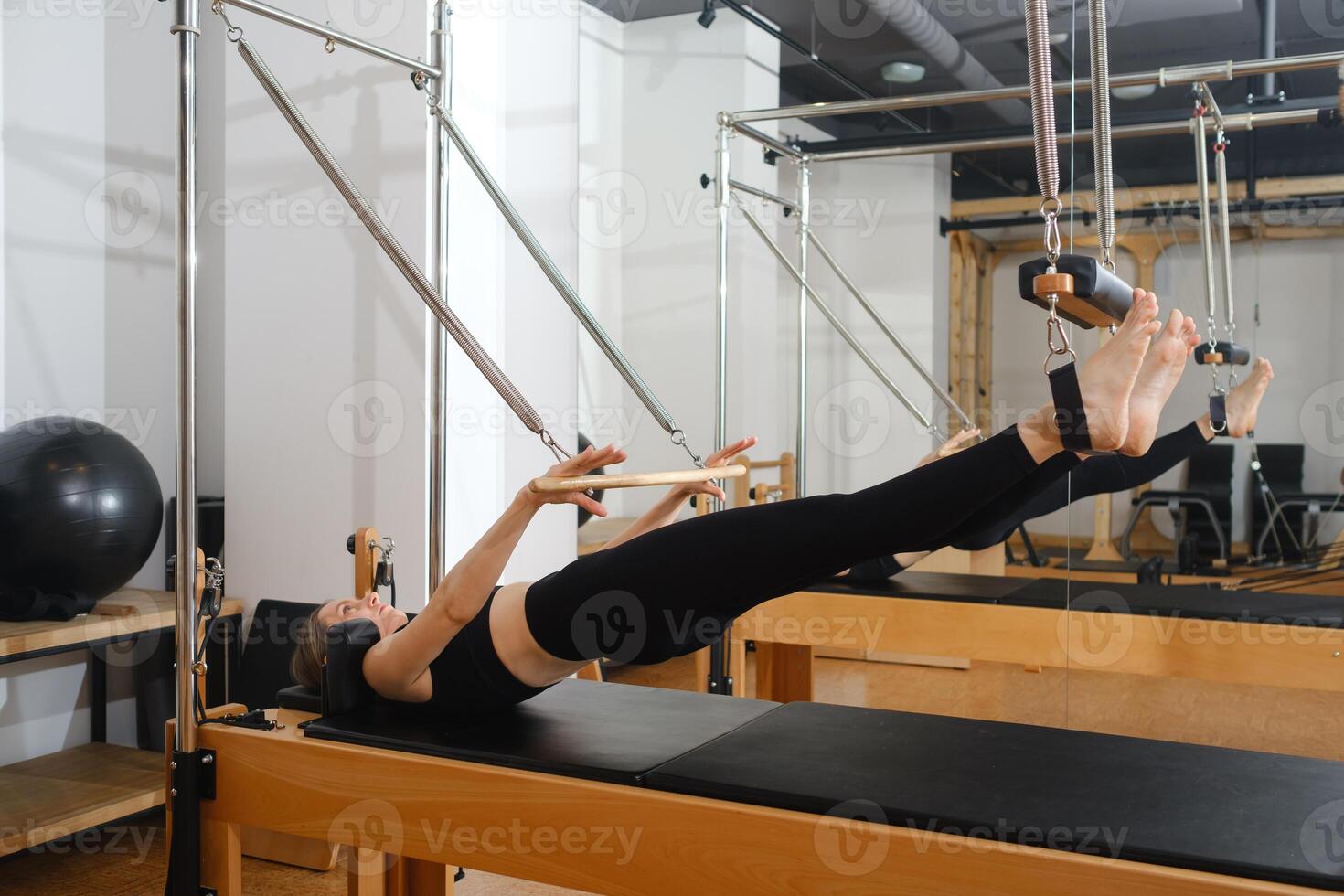 Young girl doing Pilates on trapeze table in the gym. Beautiful slim woman in black clothes performs exercises to strengthen the spine and back muscles photo