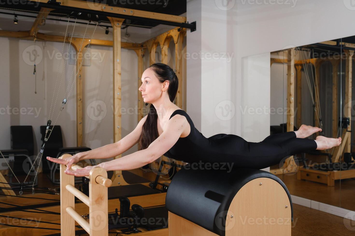 Young girl doing Pilates barre in a gym. Beautiful slim woman in black clothes performs exercises to strengthen the spine and back muscles photo