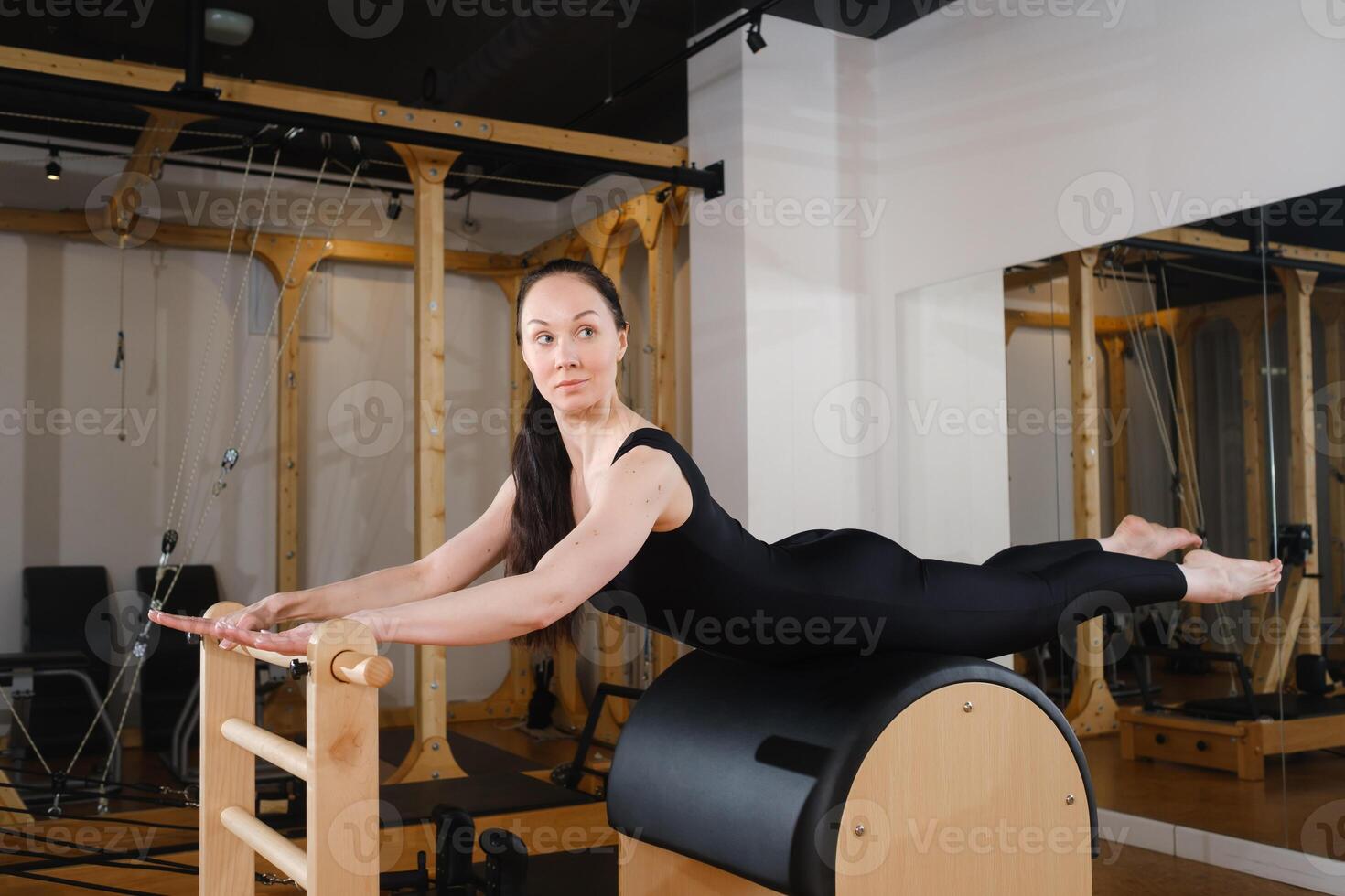 Young girl doing Pilates barre in a gym. Beautiful slim woman in black clothes performs exercises to strengthen the spine and back muscles photo