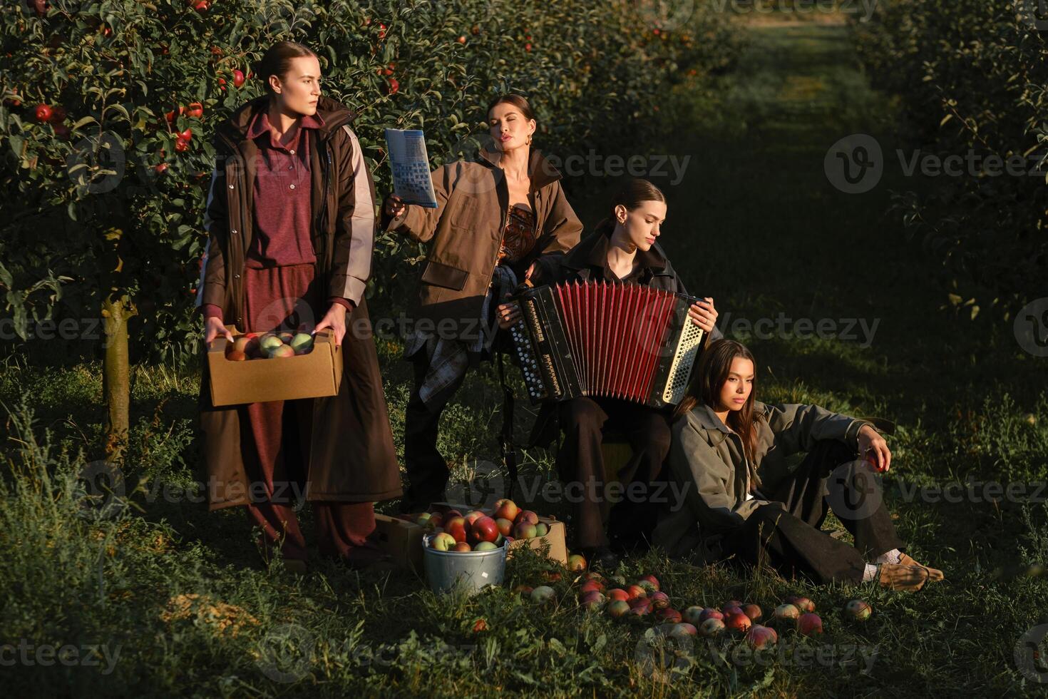 Four fashionable country girls at the apple harvest in the orchard. Happy girls playing accordion after apple harvest in an autumn orchard photo