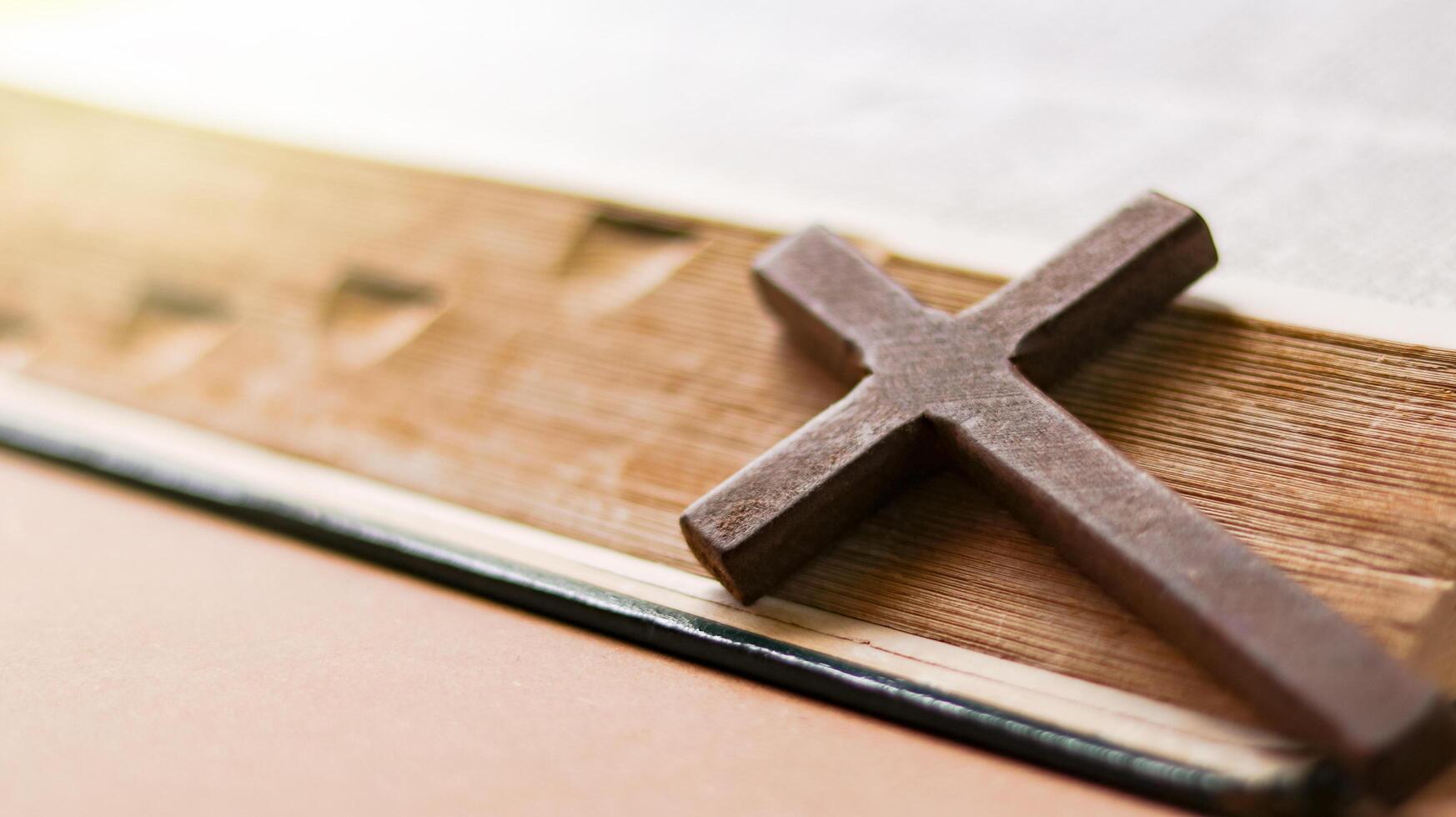 Dark red wooden cross leaning against an old open book symbolizing the spread of Jesus Christs love among Christians reflecting faith devotion and the importance of Christian teachings. photo