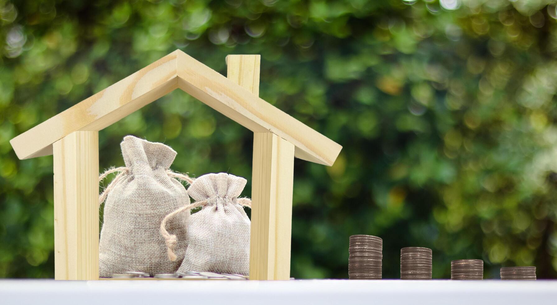 Wooden house model with burlap sacks of coins arranged inside, representing the idea of saving money to build or invest in a home. photo