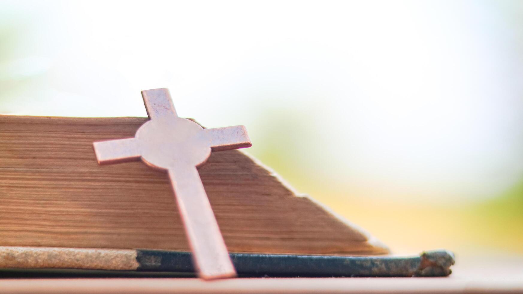 Shiny copper cross leaning against an old open book symbolizing the spread of Jesus Christs love among Christians reflecting faith devotion and the importance of Christian teachings. photo