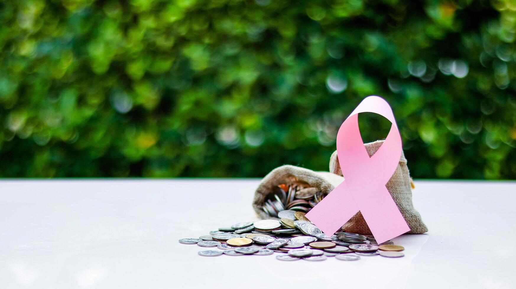 Pink ribbon, symbolizing cancer awareness, placed on a burlap sack filled with coins, representing raising awareness and supporting cancer related causes through donation funds photo