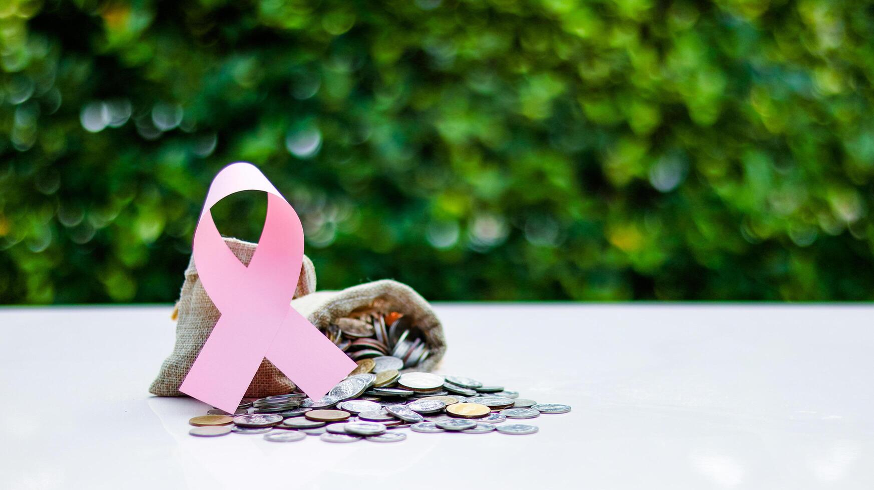 Pink ribbon, symbolizing cancer awareness, placed on a burlap sack filled with coins, representing raising awareness and supporting cancer related causes through donation funds photo