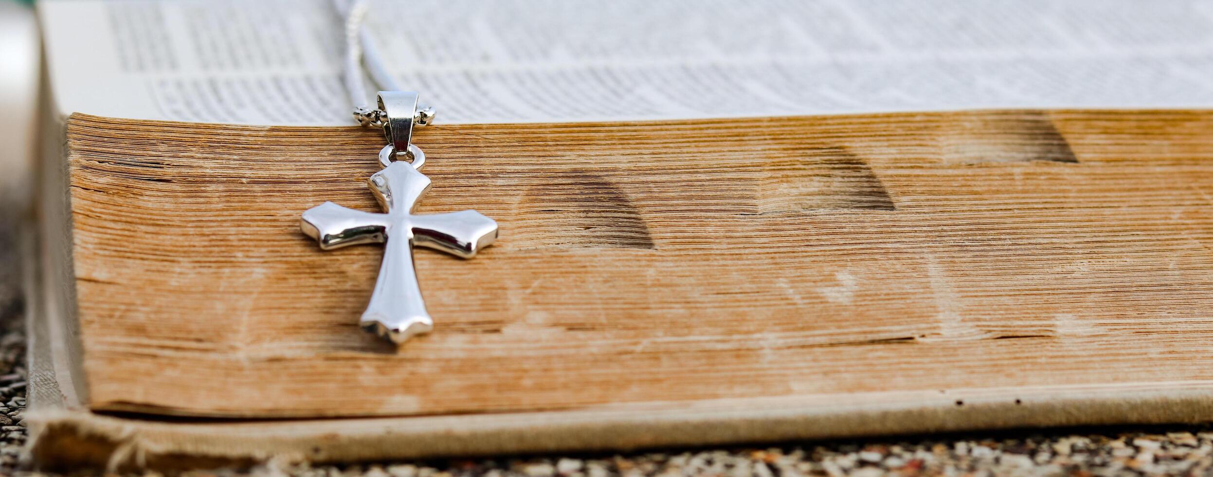 Shiny metal cross leaning against an old open book symbolizing the spread of Jesus Christs love among Christians reflecting faith devotion and the importance of Christian teachings. photo