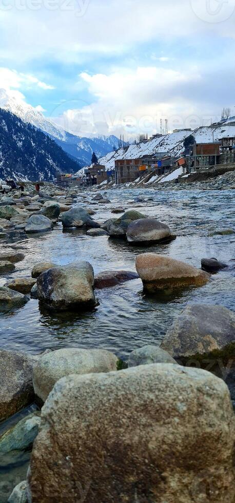 A river with rocks and snow covered mountains in the background photo