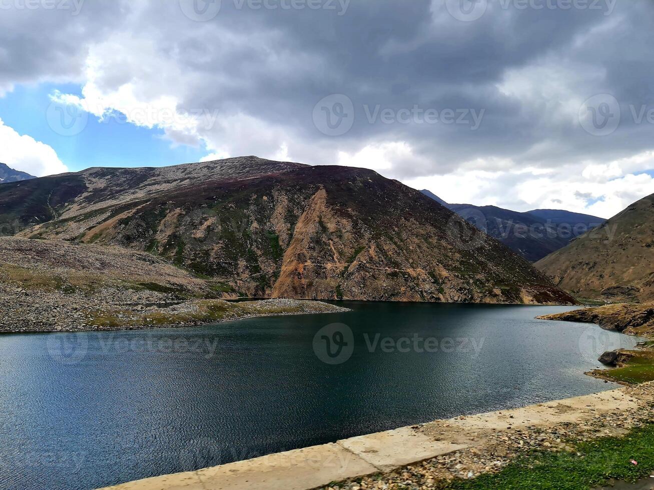 A lake surrounded by mountains and a road photo