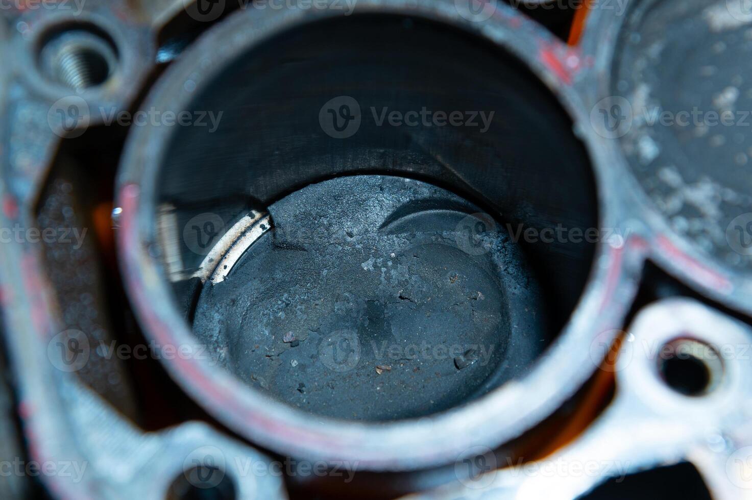 An exposed disassembled internal combustion engine. The engine block contains dirty pistons with carbon deposits and broken pieces of metal. The concept of lack of car care and untimely engine service photo
