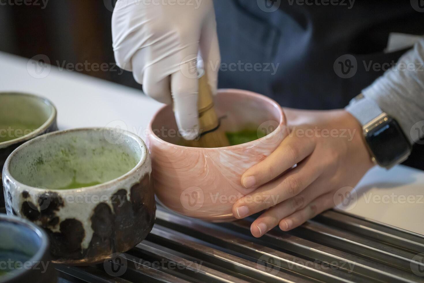 Woman whisking matcha powder while making matcha green tea with traditional accessories for tea ceremony photo