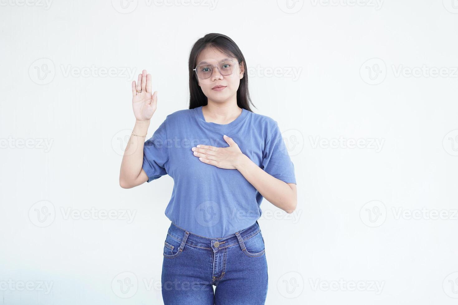 Beautiful Asian woman places her hand on her chest, making a sincere gesture of an oath or promise against a white background photo