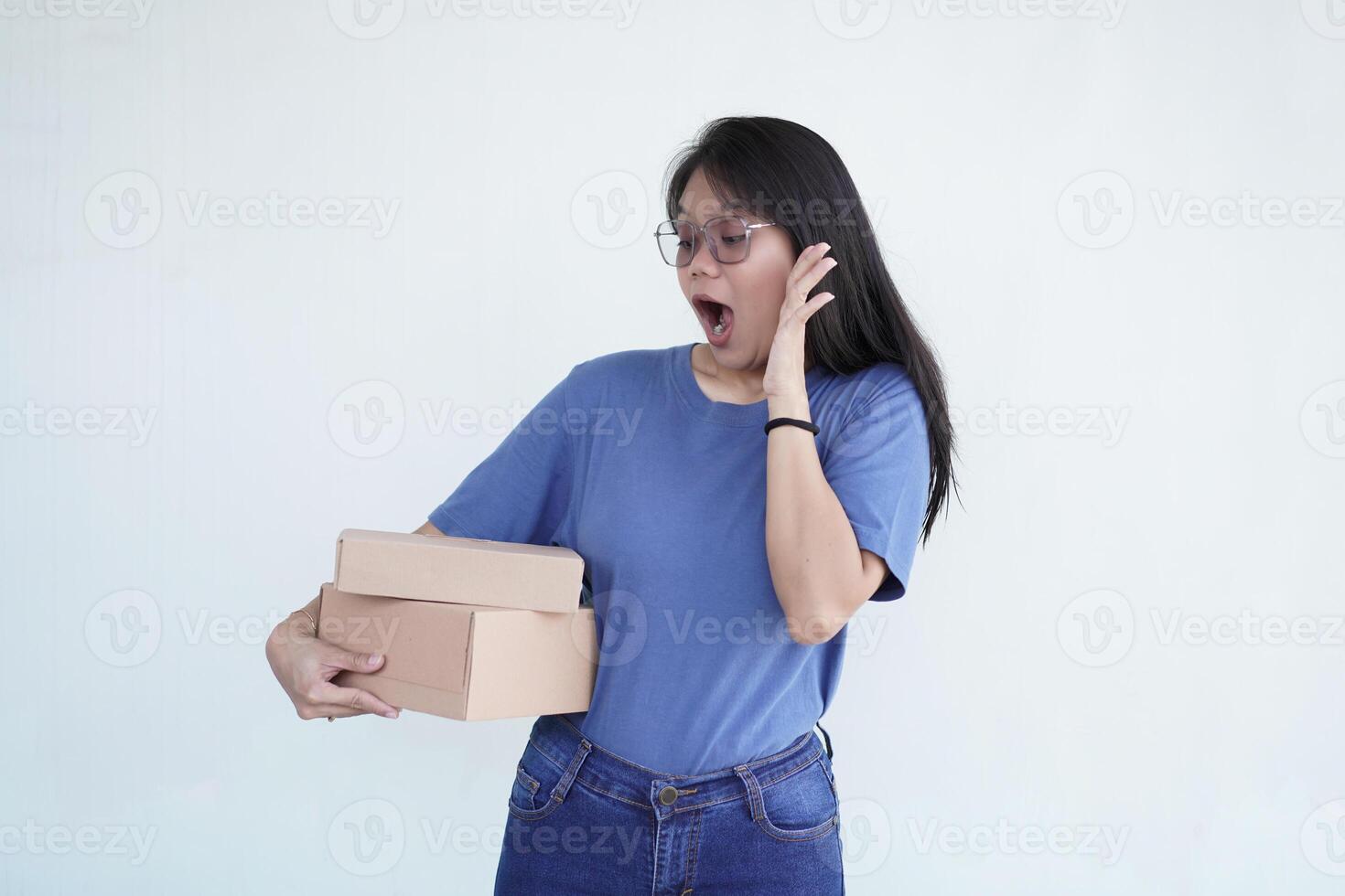 beautiful Asian woman holds a box package, displaying a shocked wow face expression against a white background photo