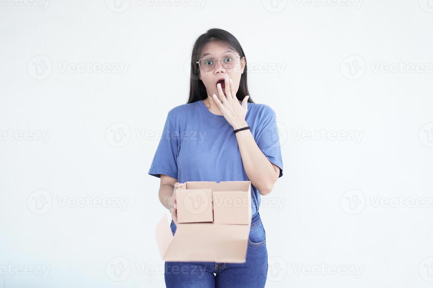 beautiful Asian woman holds a box package, displaying a shocked wow face expression against a white background photo