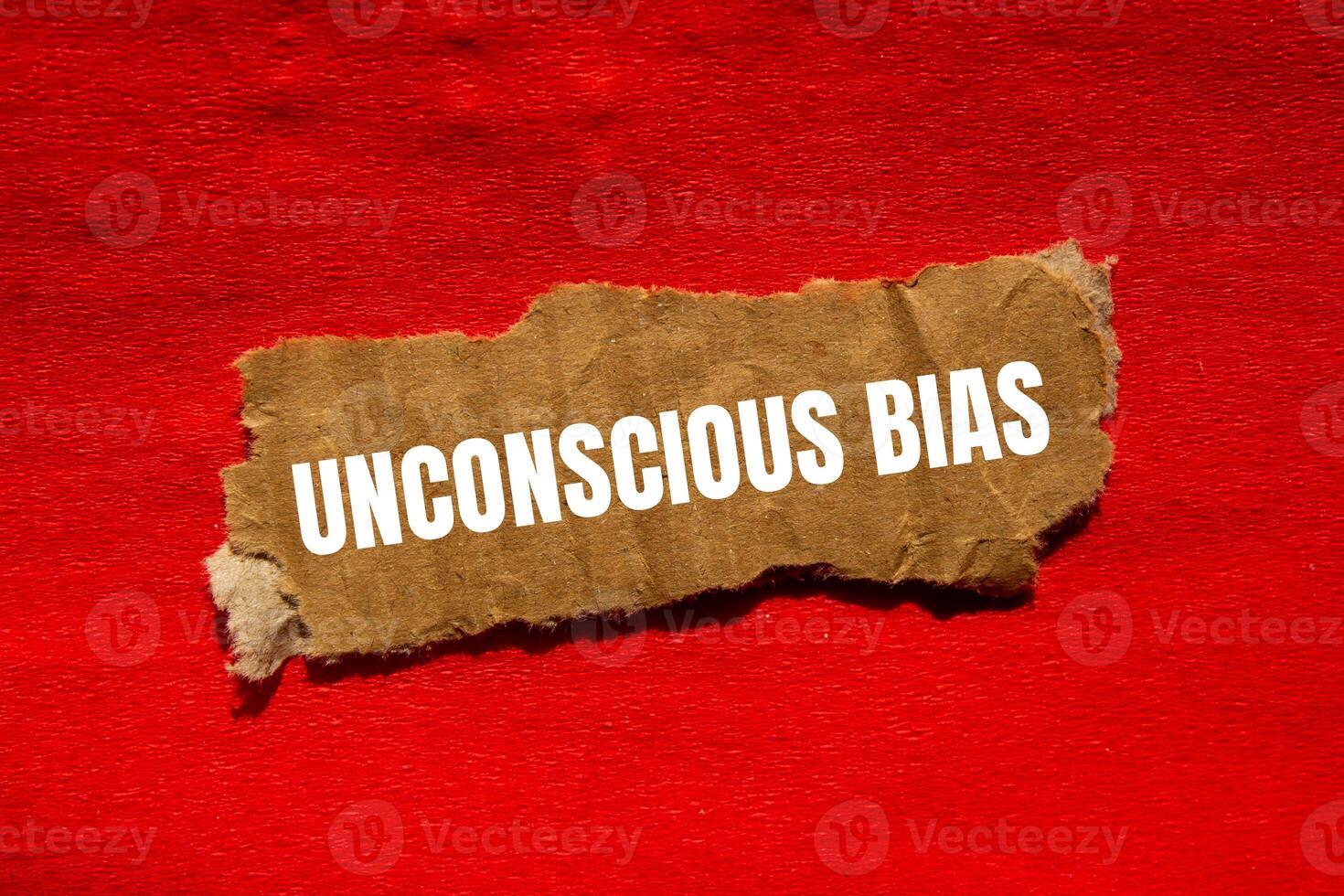 Unconscious bias message written on ripped torn cardbaord paper piece with red background. Conceptual unconscious bias symbol. Copy space. photo