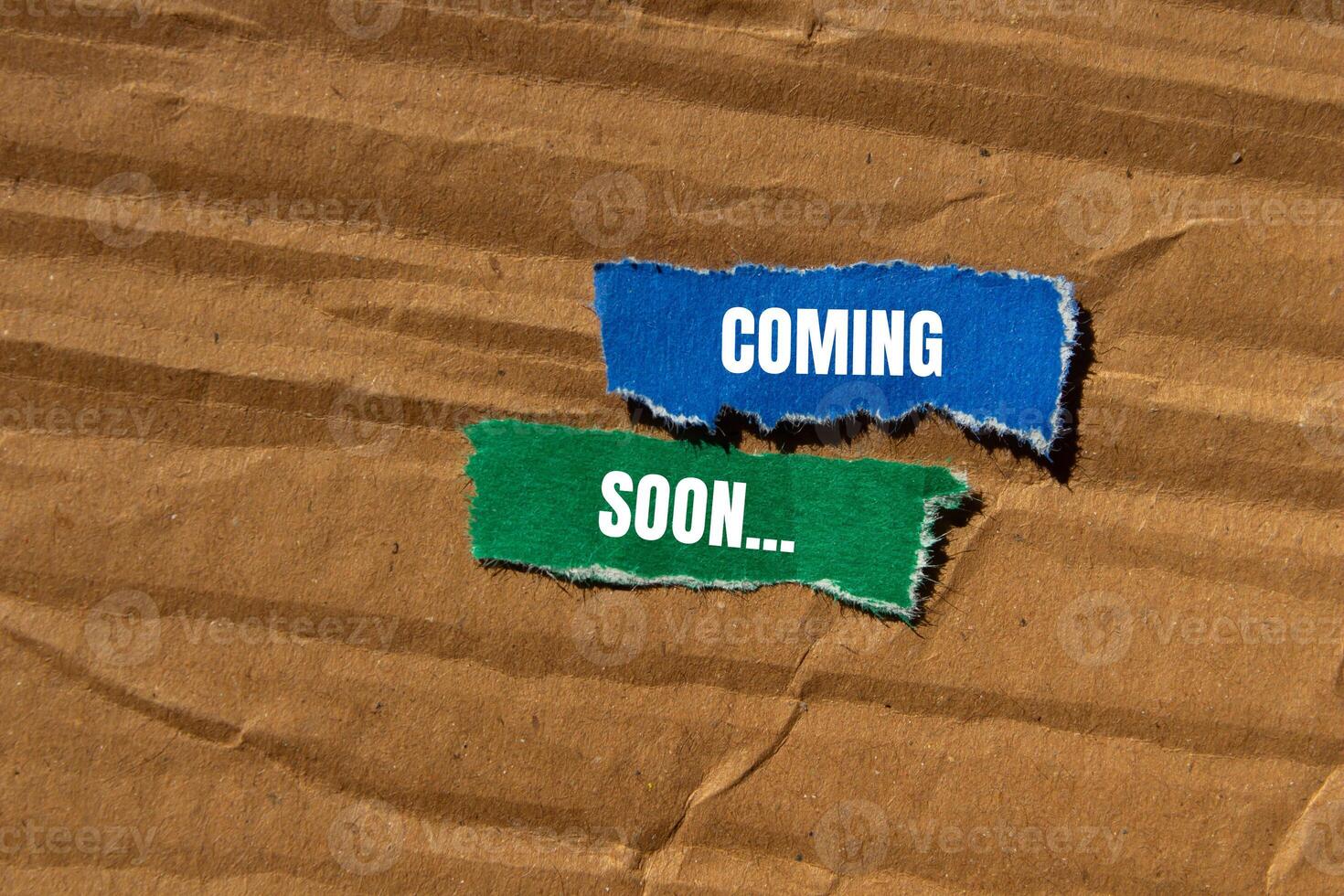 Coming soon message written on ripped torn paper pieces with cardboard background. Conceptual coming soon symbol. Copy space. photo