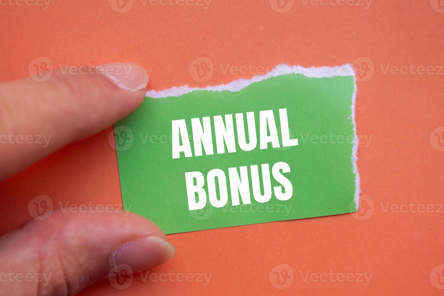 Annual bonus message written on ripped green torn paper piece with orange background. Conceptual annual bonus symbol. Copy space. photo