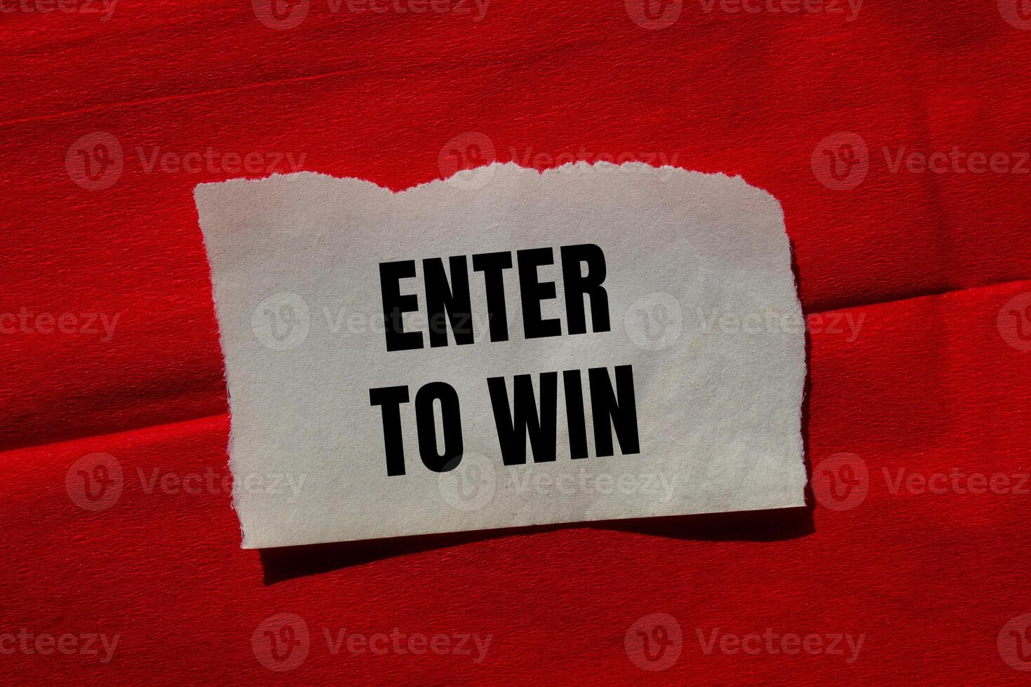 Enter to win message written on ripped torn paper piece on red background. Conceptual enter to win symbol. Copy space. photo