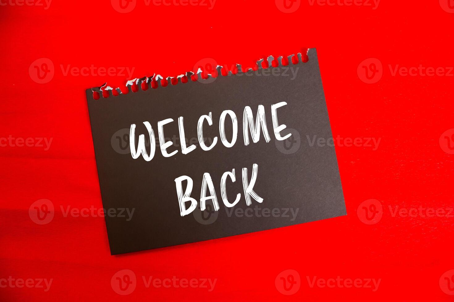 Welcome back message written on black notebook page paper with red background. Conceptual welcome back symbol. Copy space. photo
