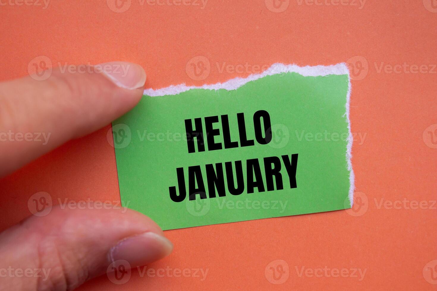 Hello january message written on ripped torn green paper piece with orange background. Conceptual hello january symbol. Copy space. photo
