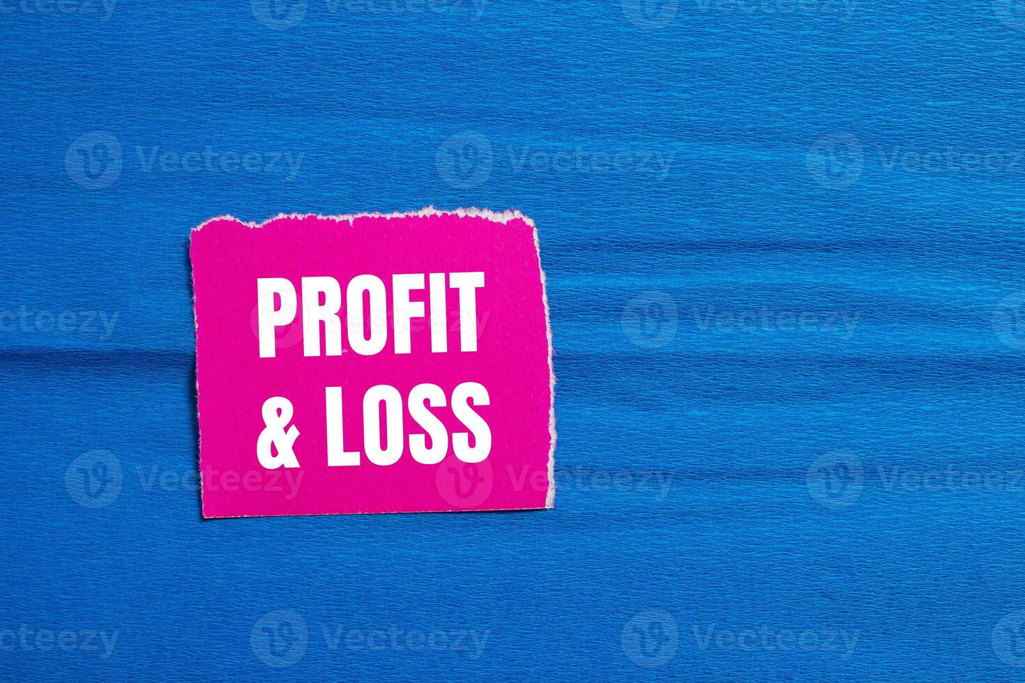 Profit and loss message written on ripped pink torn paper piece with blue background. Conceptual profit and loss symbol. Copy space. photo