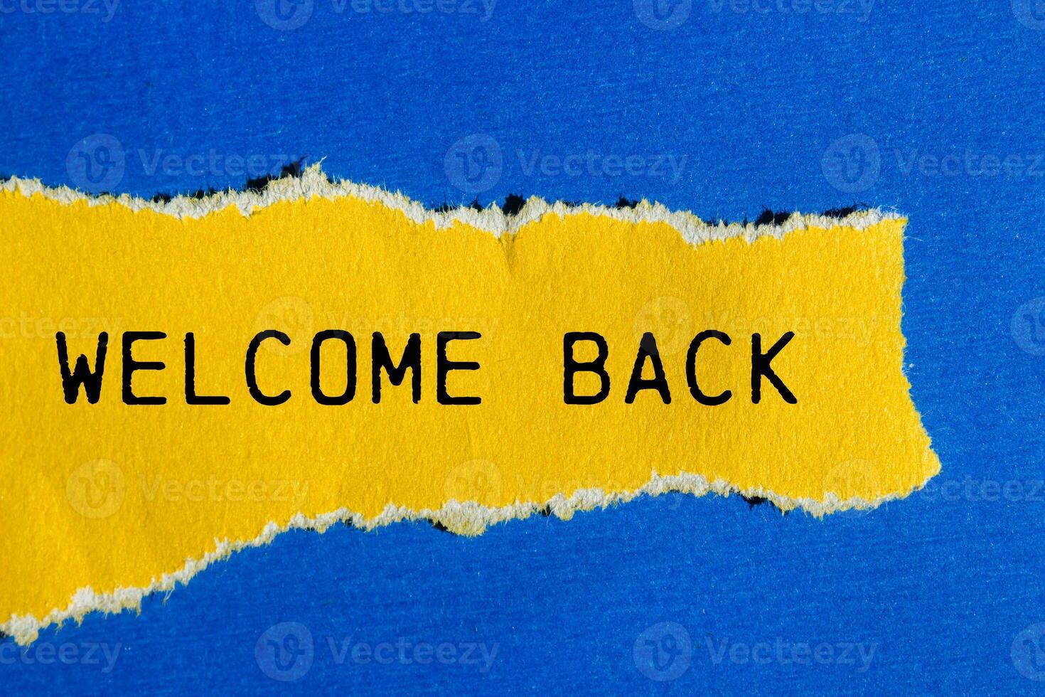 Welcome back message written on ripped torn yellow paper piece with blue background. Conceptual welcome back symbol. Copy space. photo