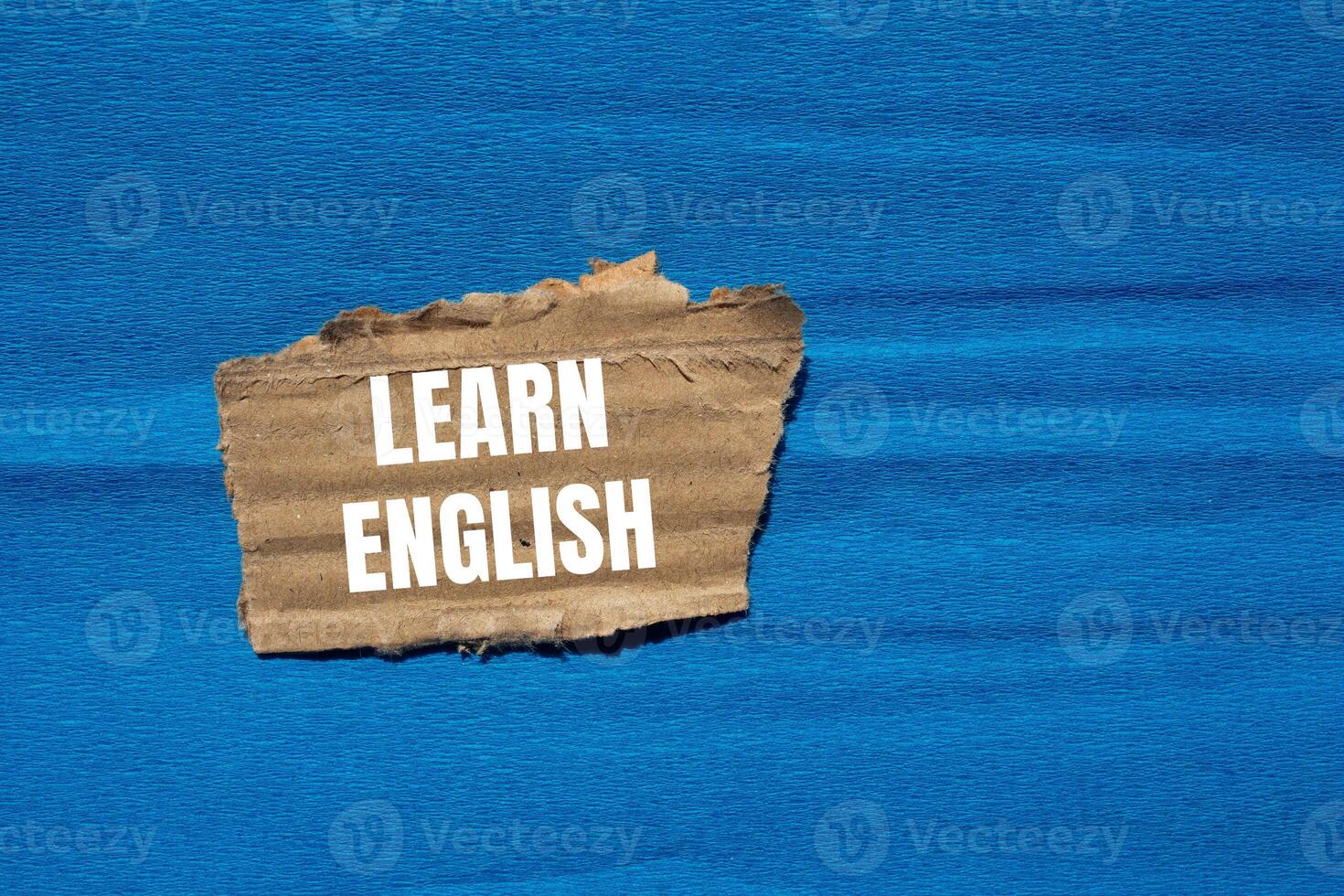 Learn english message written on ripped torn cardboard paper piece with blue background. Conceptual learn english symbol. Copy space. photo