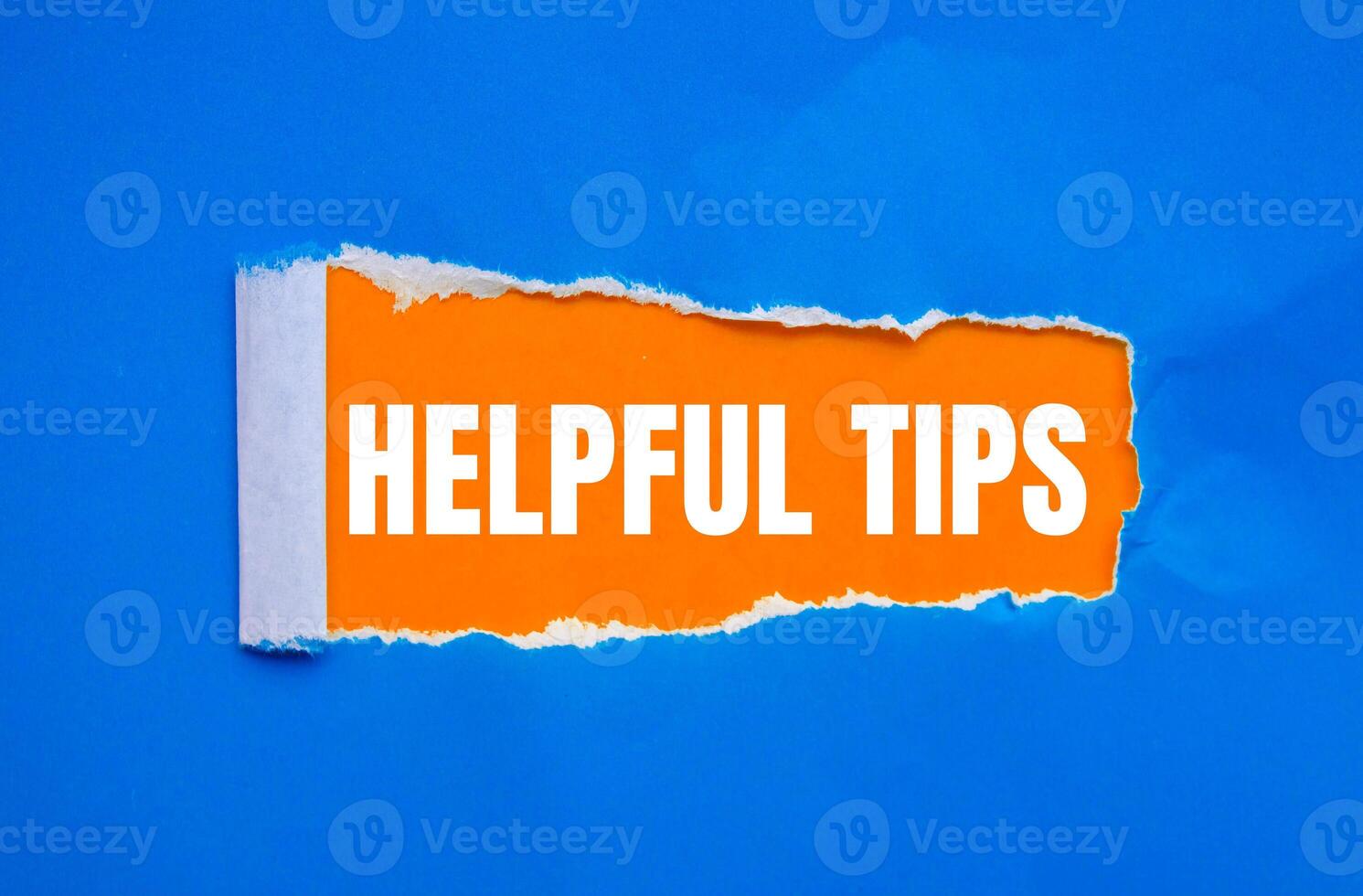Helpful tips message written on ripped torn blue paper with orange background. Conceptual helpful tips symbol. Copy space. photo