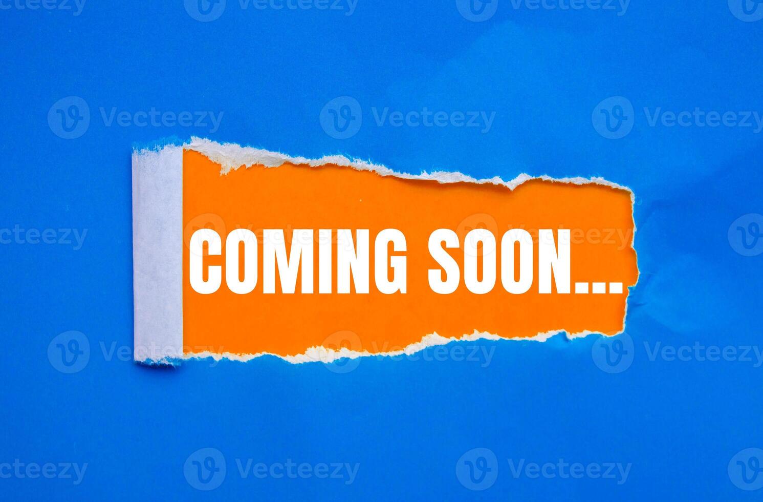 Coming soon message written on ripped torn blue paper with orange background. Conceptual coming soon symbol. Copy space. photo