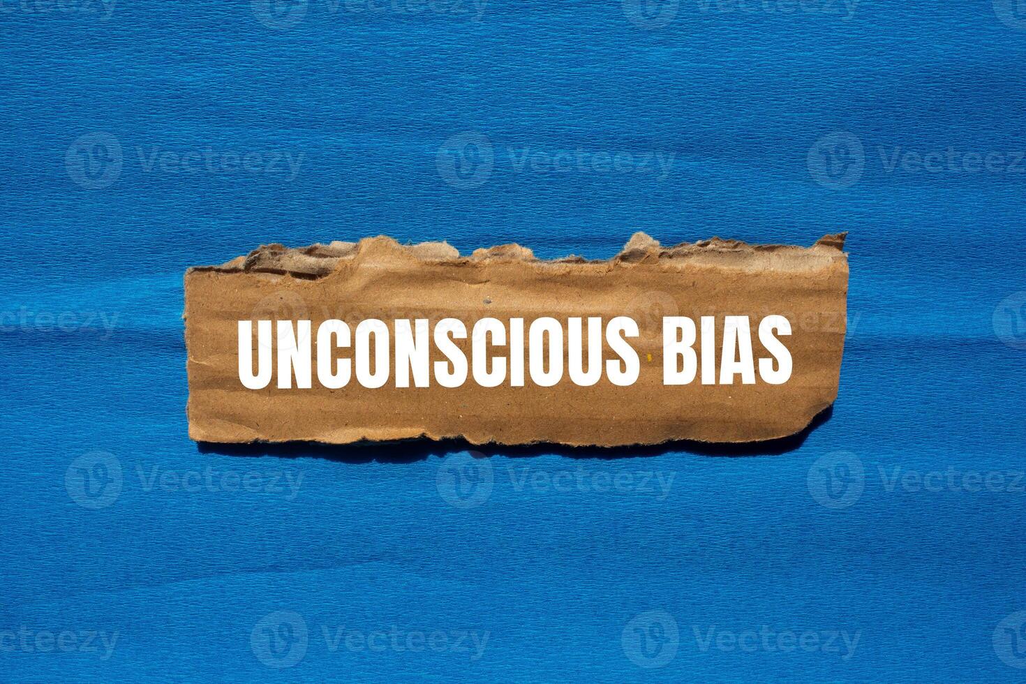 Unconscious bias message written on ripped torn cardboard paper piece with blue background. Conceptual unconscious bias symbol. Copy space. photo