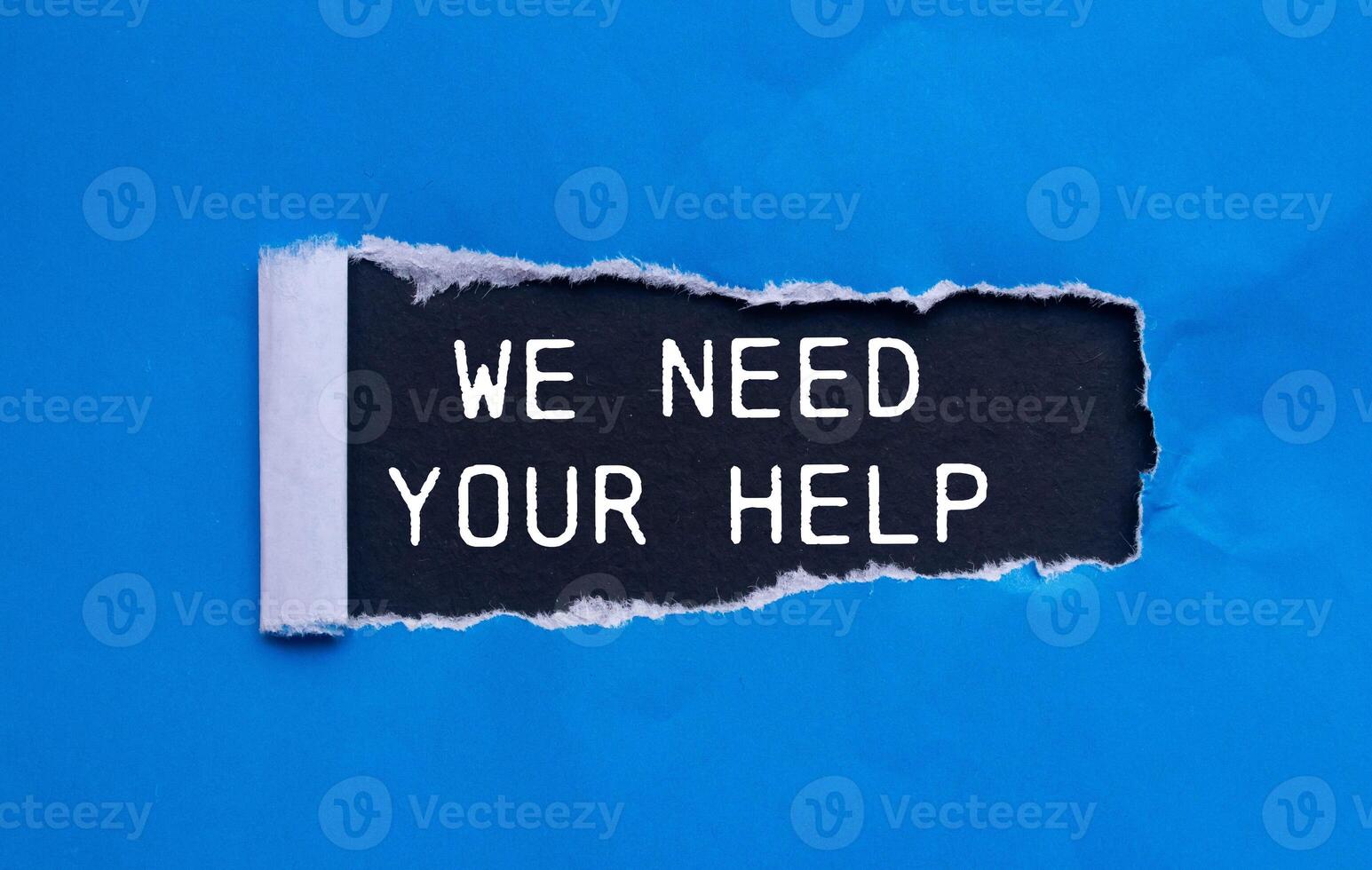 We need your help message written on ripped torn blue paper with black background. Conceptual we need your help symbol. Copy space. photo