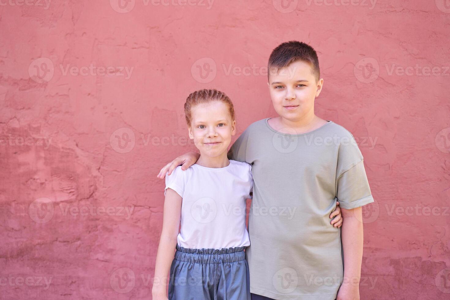 Siblings smiling together in front of a red wall outdoors on a sunny day. photo