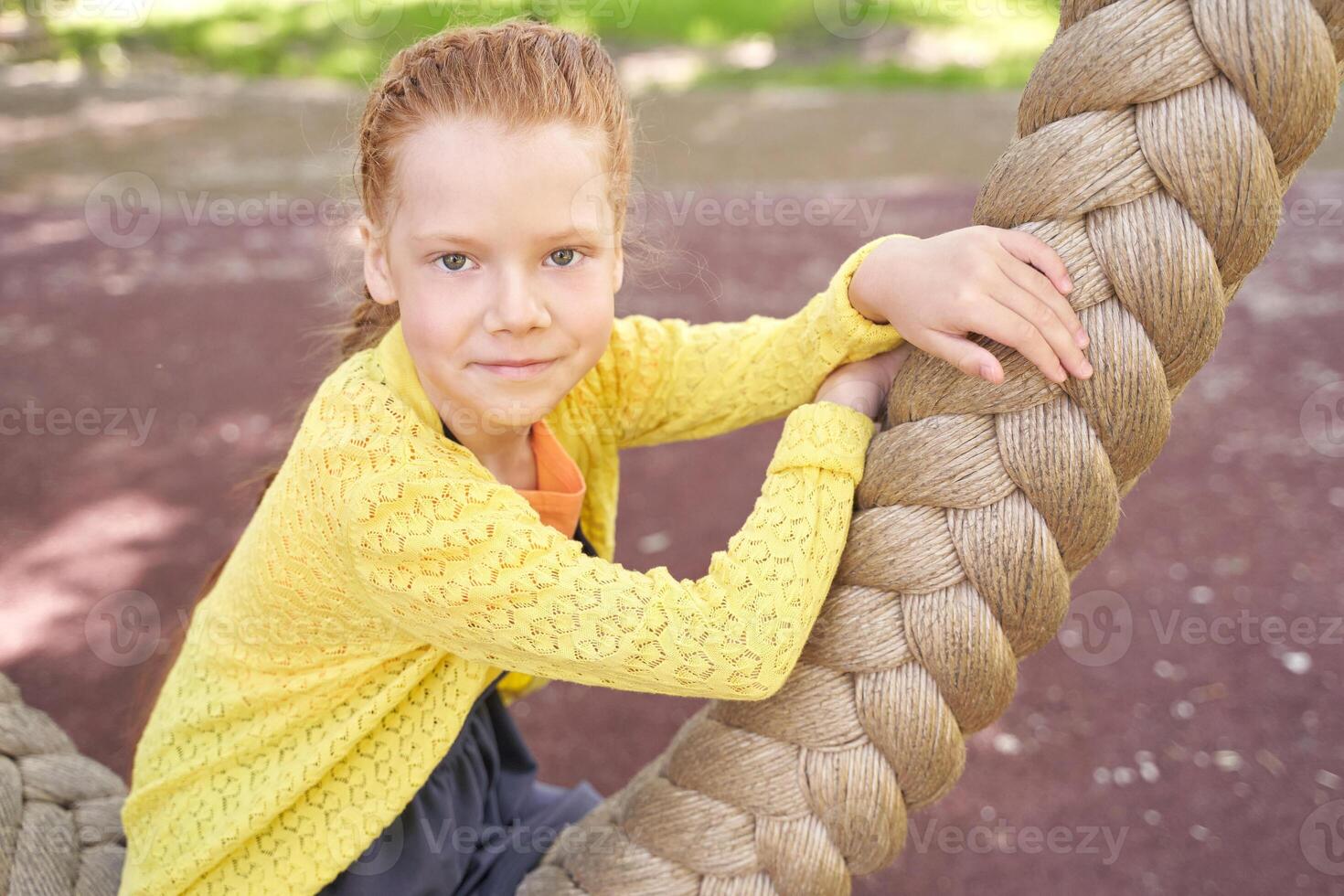 Young girl climbing rope outdoors in playful yellow sweater at sunny playground. photo