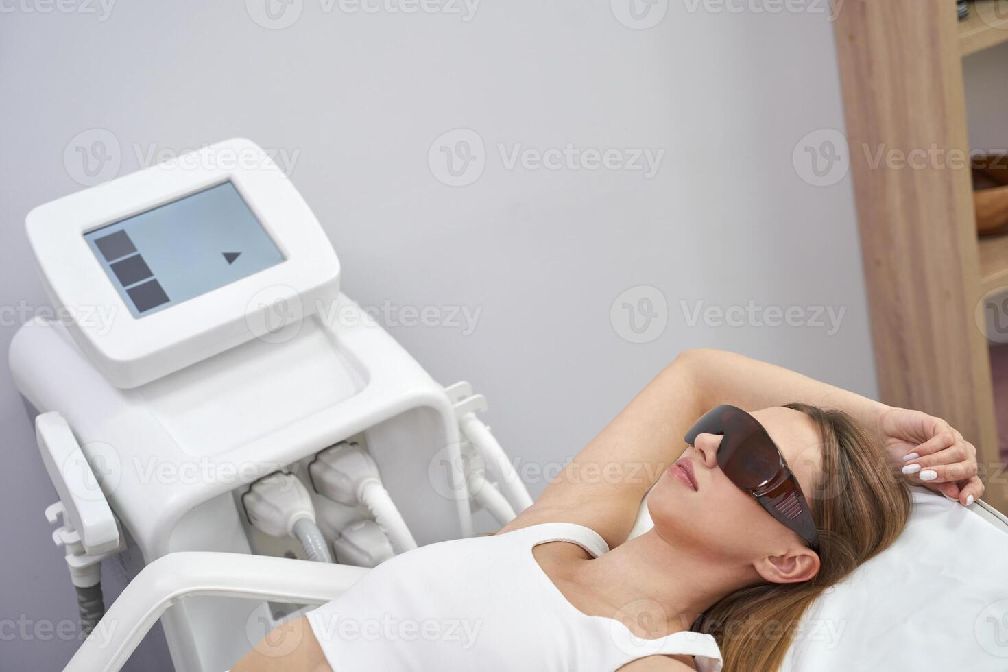 Woman undergoing laser hair removal treatment in modern clinic with protective goggles and advanced equipment. photo