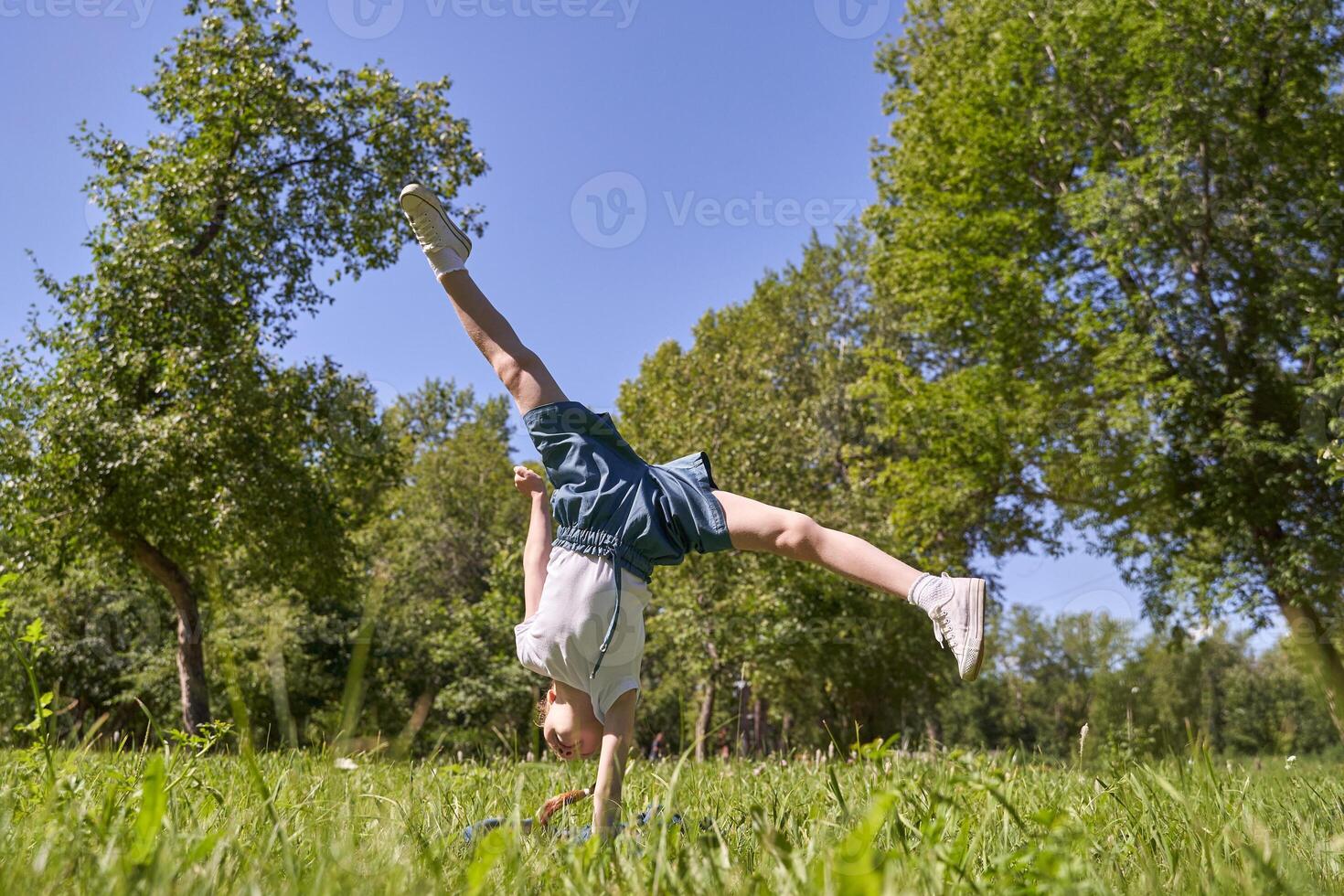 Joyful child performing cartwheel in sunny park surrounded by lush greenery and bright blue sky. photo