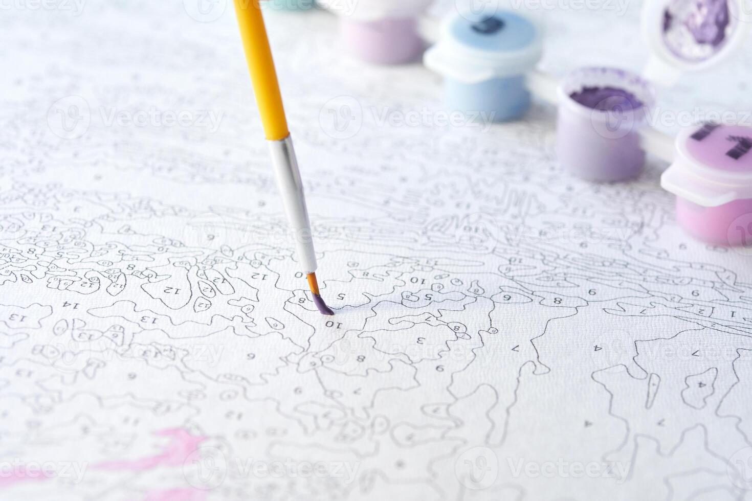 Coloring by numbers. close-up of a paintbrush hovering above a numbered canvas with paint pots in soft pastel colors. photo