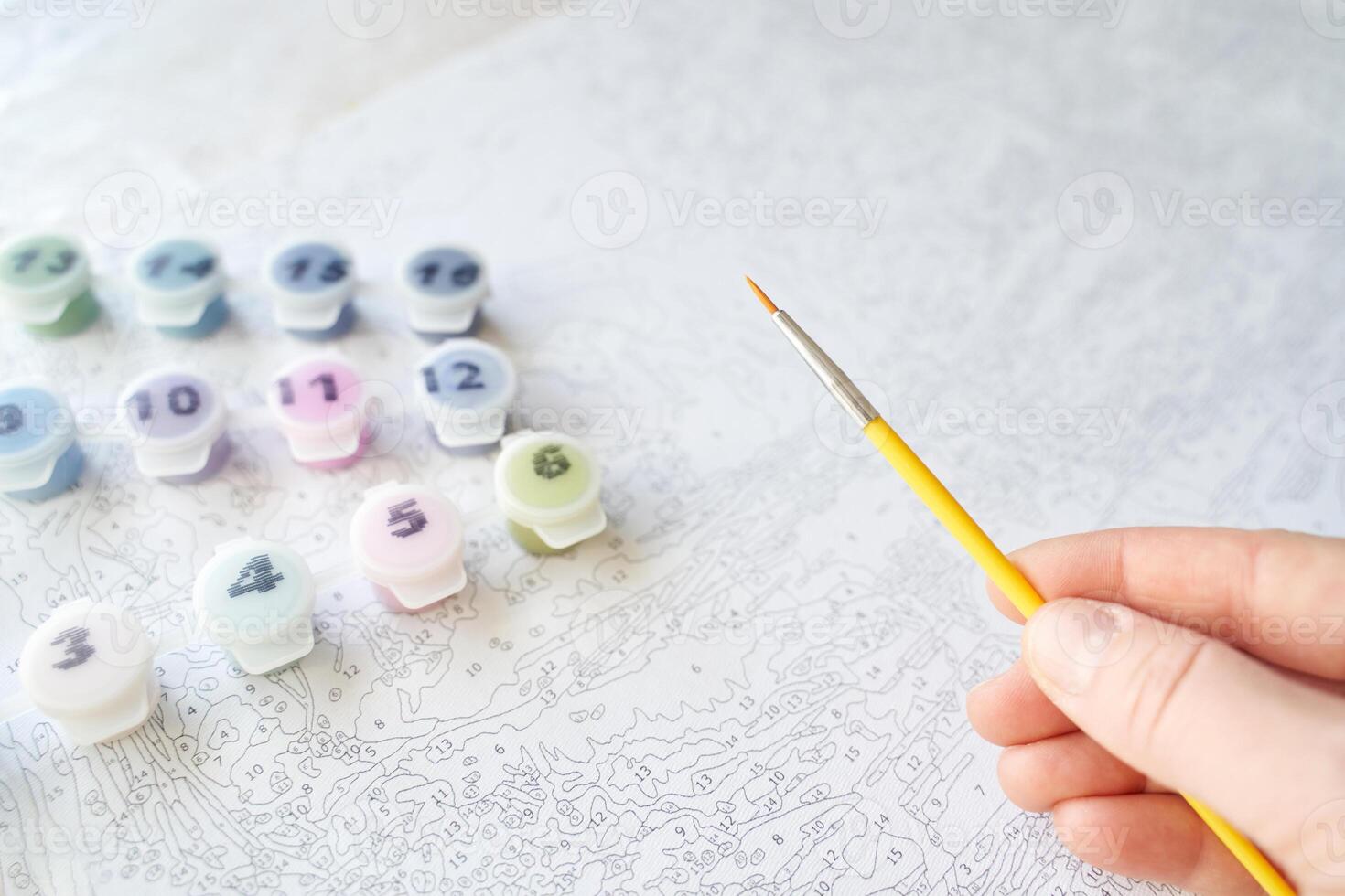 Hand holding brush over paint by numbers canvas with colorful paint pots for creative diy art and relaxation. photo
