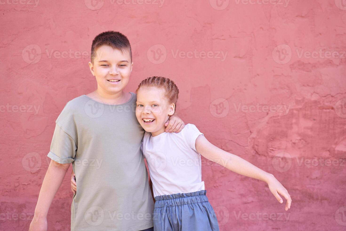 Happy siblings hugging in front of pink wall on a sunny day. photo